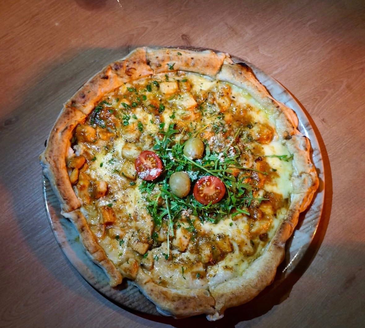Stone-baked pizza topped with arugula, cherry tomatoes and olives